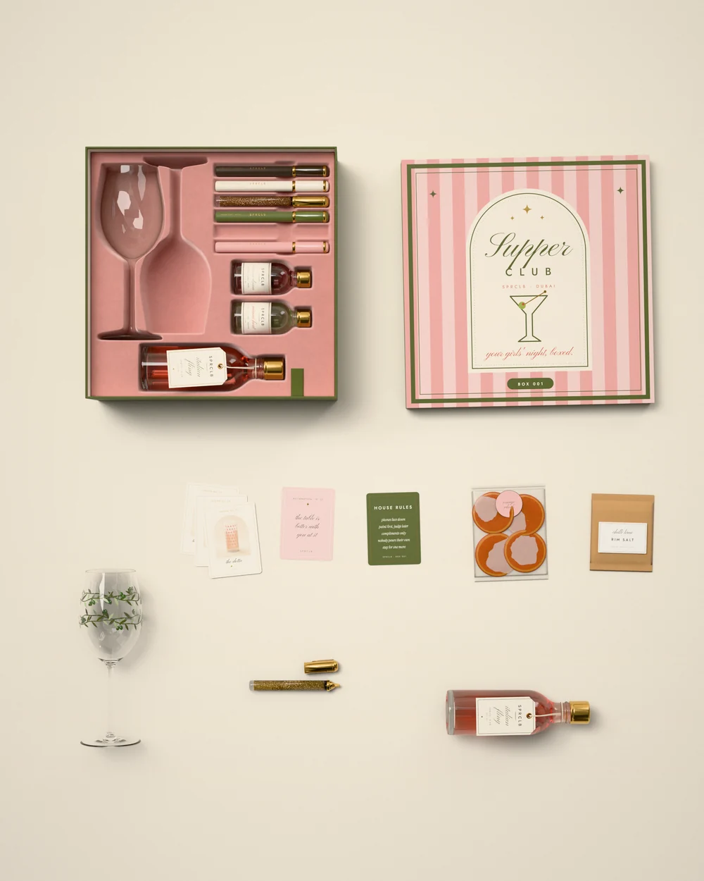 Everything in Box 001 laid out from above: the open box with a glass, paint pens and three pours in its velvet insert, the pink-striped Supper Club lid, a glass painted with a leafy vine, design and affirmation cards, the house-rules card, orange wheels, chilli-lime rim salt and a bottle of Italian Fling