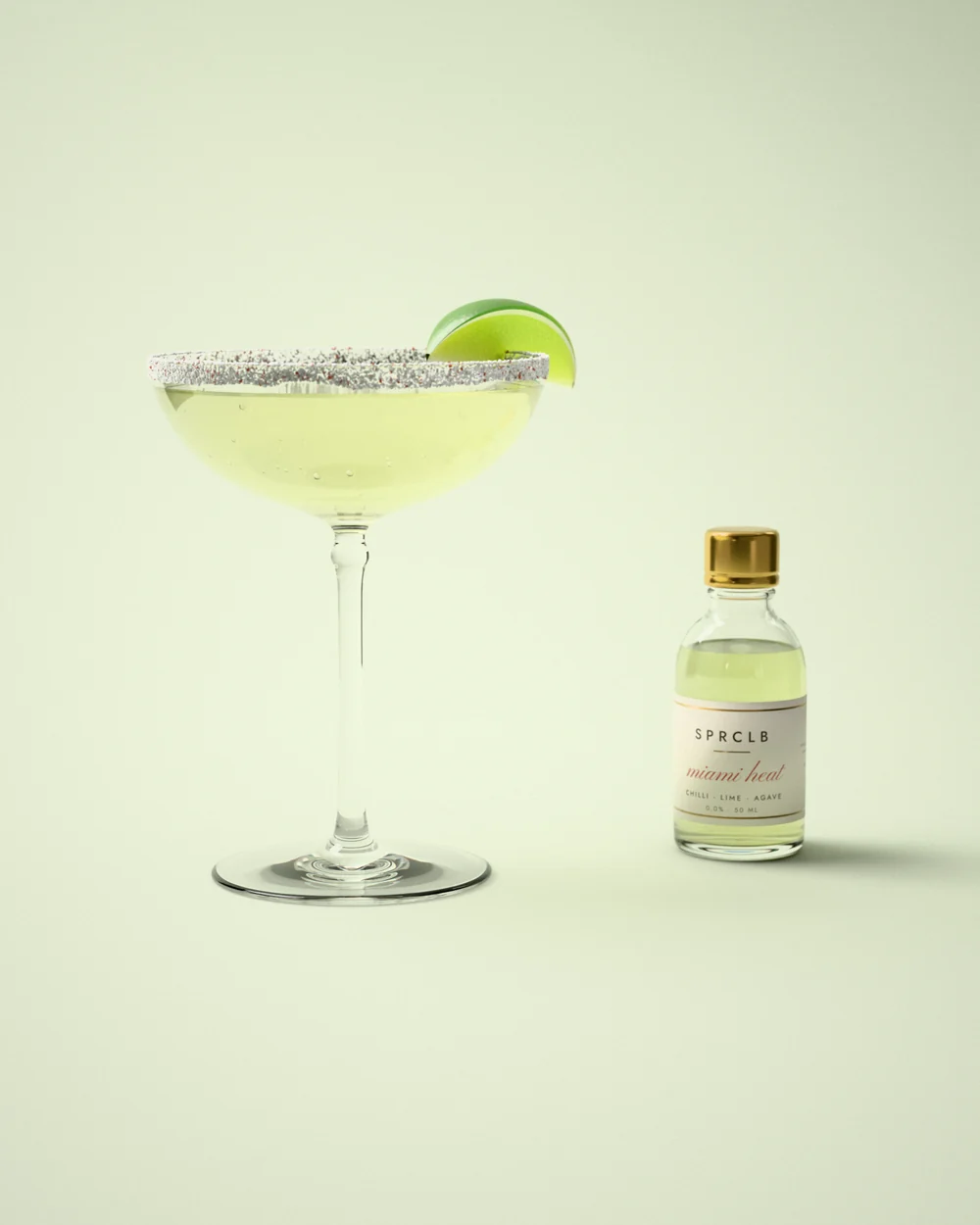 Miami Heat: a pale lime cooler in a coupe glass with a chilli-salt rim and a wedge of lime, beside a small clear SPRCLB syrup bottle