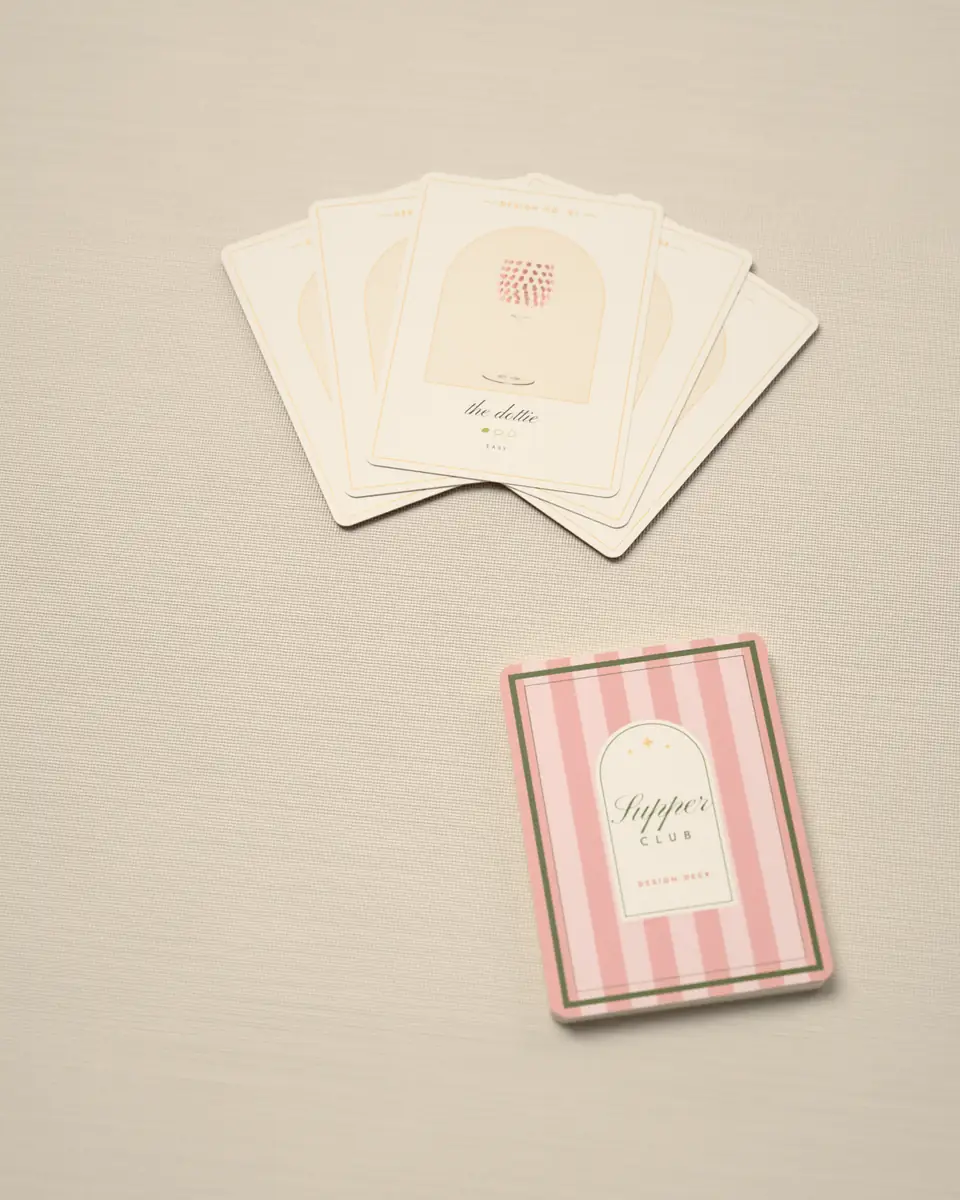 The design deck: five SPRCLB design cards fanned on linen, each with a painted glass in its arch, the striped deck box beside them