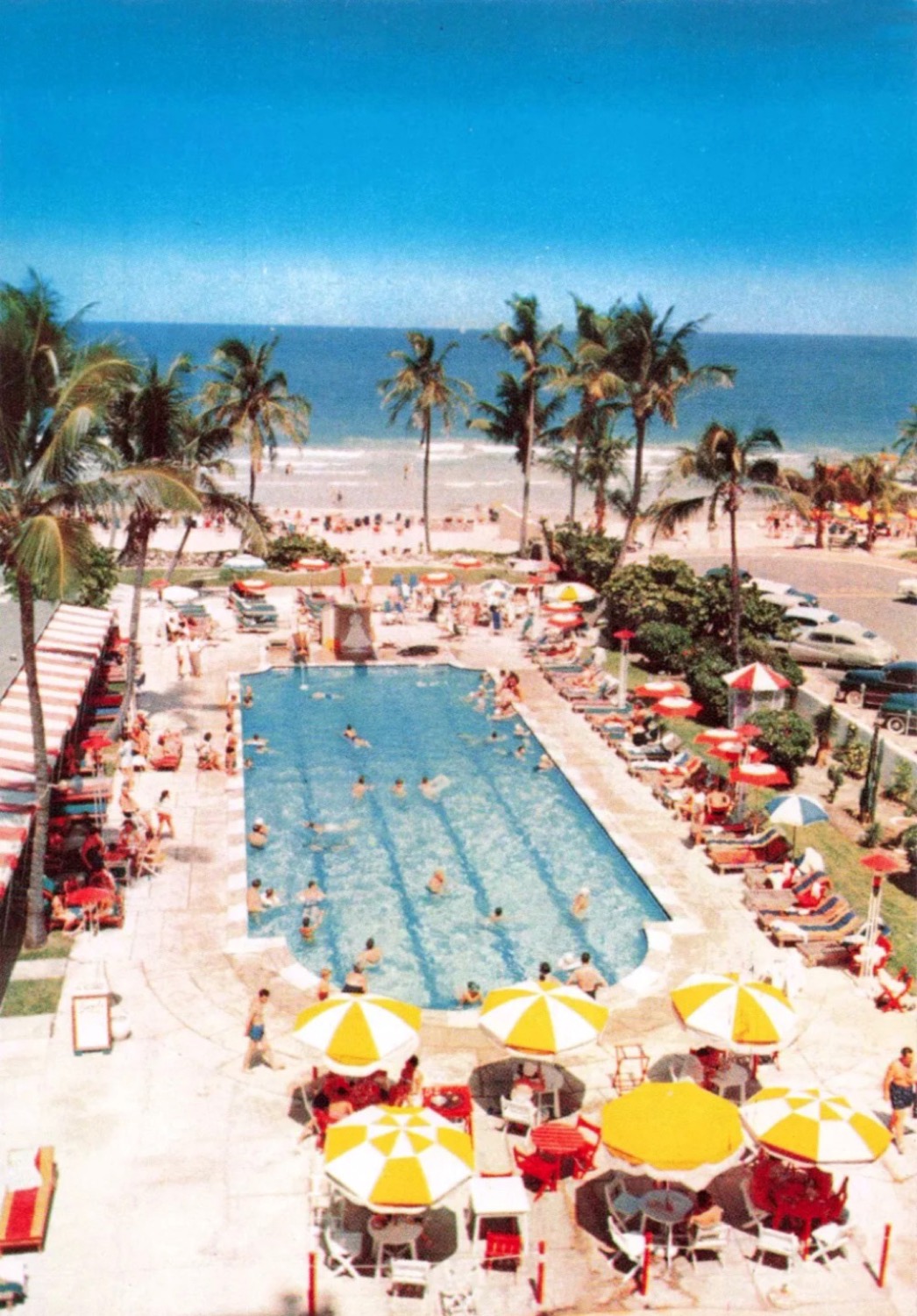 1950s postcard looking down the Sands Hotel pool in Miami Beach, yellow and white umbrellas along the deck